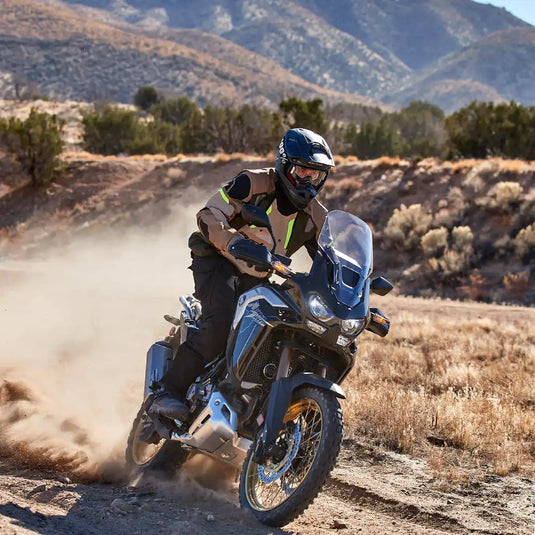 Una motocicleta de aventura con un piloto con equipo de protección, levantando polvo en un sendero de tierra.