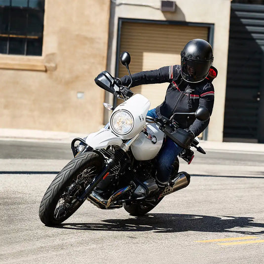 Motocicleta blanca con un motorista que lleva un casco y una chaqueta negros.