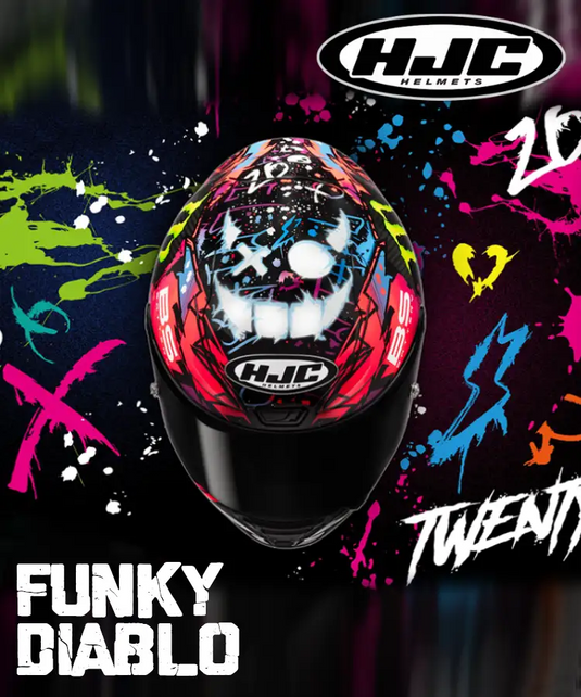 Un casco de motocicleta vibrante con estilo de graffiti, con base negra y salpicaduras audaces de pintura roja, rosa, azul, verde y amarilla, que presenta un diseño de cara de diablo estilizada.