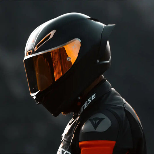 Casco de motocicleta negro mate con visera de tonalidad naranja y traje de carreras a juego.