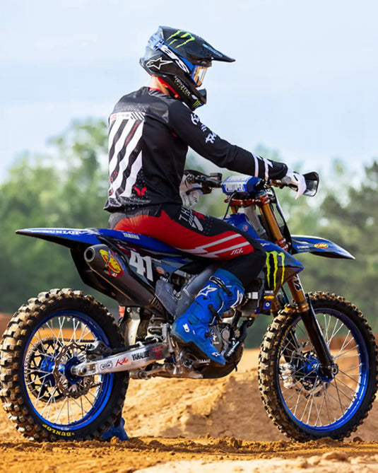Un piloto de motocross con un traje de carrera completo en una moto de tierra azul y negra.