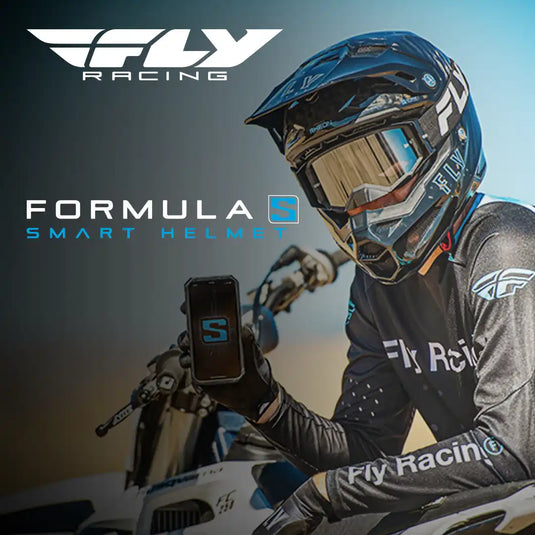 Una persona con un casco y camiseta de dirt bike negra, sosteniendo un teléfono inteligente.